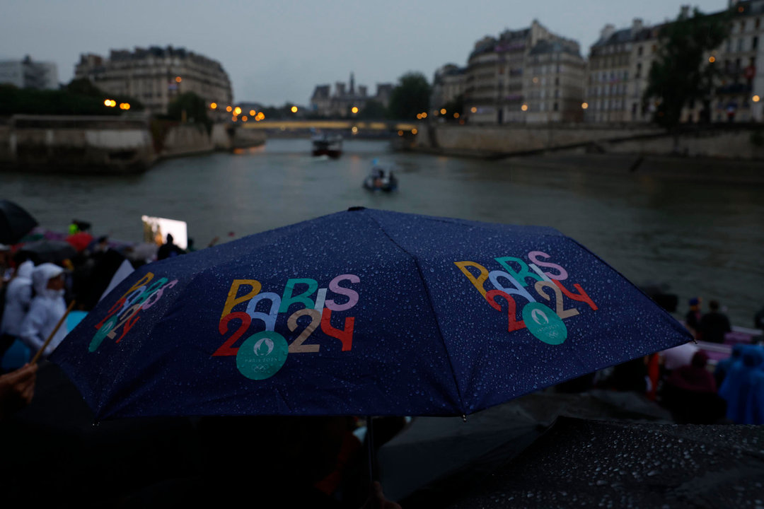 Miembros del público se protegen de la lluvia con paraguas mientras observan el desfile de las delegaciones por el río Sena, durante la ceremonia de inauguración de los Juegos Olímpicos de París 2024, este viernes en la capital francesa. EFE/Julio Muñoz