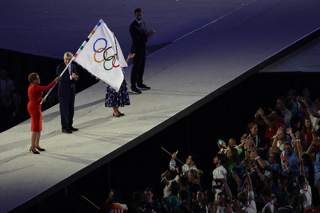 La alcaldesa de Los Angeles, Karen Bass (i), ondea la bandera olímpica, junto al presidente del COI, Thomas Bach (c), durante la ceremonia de clausura de los Juegos Olímpicos de París 2024 celebrada este domingo, en el Estadio de Francia en Saint-Denis (Francia).EFE/ Miguel Gutiérrez